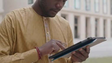 Şehir merkezinde dijital tablet kullanan, ofisten uzakta çalışan genç siyahi bir adamın belini kaldırın.