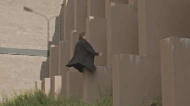 Akrobatik, siyah elbiseli, beton duvardan ters takla atan beyaz bir adam.