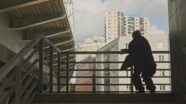 Aktif genç beyaz adam endüstriyel alandaki açık hava merdivenlerinde akrobatik parkur hareketleri yapıyor.