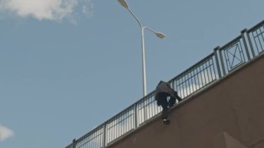 Siyah elbiseli çevik bir adamın açık havada parkçılıkla uğraşırken duvardan aşağı inişi geniş açılı bir bakış açısı.