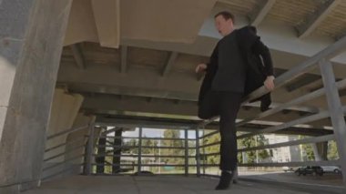 Siyah elbiseli akrobatik genç adam gündüz vakti dışarıda parkur yaparken beton duvardan ters takla atıyor.