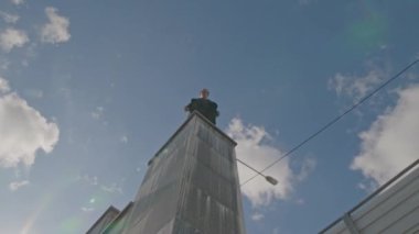 Açık mavi gökyüzünün altında yüksek sütunlarda duran parkçı adamın düşük açılı görüntüsü.