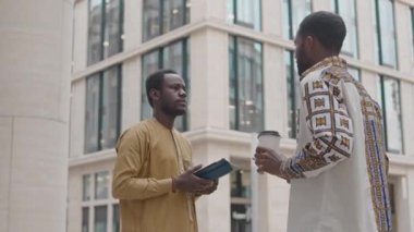 Çağdaş ofis binasının önünde dikilen iki Afrikalı Amerikalı erkek arkadaşın orta boy görüntüsü.