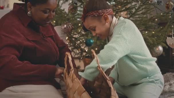クリスマスのためのアパートを一緒に飾っている間 ウィッカーバッグでクリスマスツリーのおもちゃを探しているママとアフリカ系アメリカ人の女の子の中型ショット — ストック動画