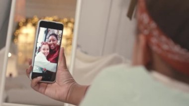 Küçük kızı olan genç siyahi bir kadının, Noel için apartmanı dekore ederken kameraya sarıldıkları selfie videolarını çekerken çekilmiş omuz üstü fotoğrafı.