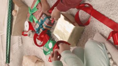 Küçük kızı, Noel hediyesinin etrafına kırmızı kurdele bağlayıp, sıcak bir dairede tatile hazırlanırken, tanınmayan bir kadının dikey çekimi.