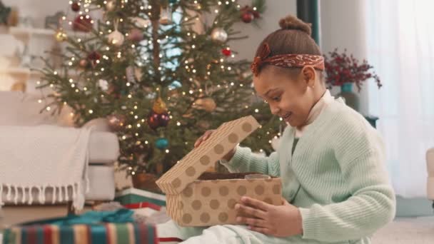 Ενθουσιασμένο Αφρικανικής Αμερικής Κοριτσάκι Ξεπακετάρισμα Χριστουγεννιάτικο Δώρο Ενώ Κάθεται Από — Αρχείο Βίντεο