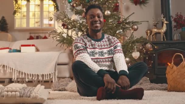 Portret Zachwyconego Młodego Afroamerykanina Ubranego Biały Świąteczny Sweter Siedzącego Podłodze — Wideo stockowe