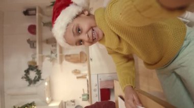 Kırmızı Noel Baba şapkası takan güzel Afrikalı Amerikalı bir kızın, annemle evde Xmas vlog kaydederken çekilmiş el kamerası görüntüsü.