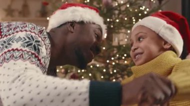 Afrika kökenli Amerikalı baba ve küçük kızı el ele tutuşup Noel ağacının yanında dans ediyorlar.