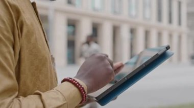 Dijital tablet üzerinde gezinen genç ve ciddi siyahi bir adam şehir merkezinde ofis dışında çalışırken