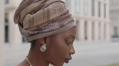 Sarıklı güzel Afro-Amerikan bir kadının şehir ortamında bulanık arka planda dikilirken yukarı ve etrafa bakınışını aşağı eğ.