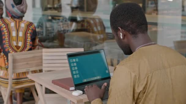 Widok Tyłu Czarny Człowiek Słuchawkach Bezprzewodowych Pomocą Laptopa Podczas Pracy — Wideo stockowe