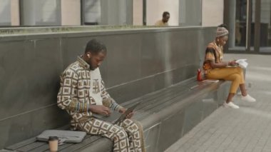 Genç Afrikalı Amerikalı bir adam elektrikli scooter kullanırken iş arkadaşıyla buluşuyor. Şehir ortamında bankta çalışıyor.