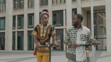 Gündüz vakti şehir merkezinde sokakta yürürken, e-scooterlı birkaç iş arkadaşının orta boy fotoğrafı.