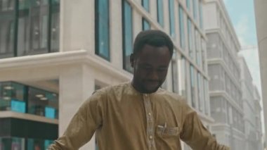 Gündüz vakti şehir merkezindeki modern ofis binasına karşı kamera karşısında dans eden neşeli genç siyahi adamın belini kaldırın.