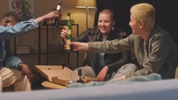 多様な友人のグループのミディアムショットビールボトルを飲みながら夜の自宅パーティーで一緒に時間を過ごしながらチャット — ストック動画