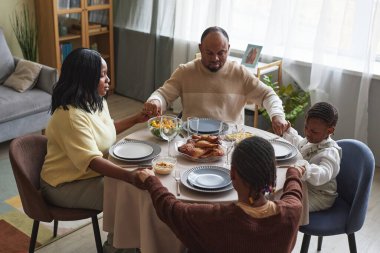 Çocuklu Afrikalı bir aile yemek masasında gözleri kapalı ve evde tatil yemeği öncesi dua ediyor.