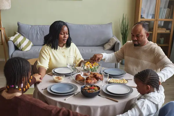 这家四口人的非洲家庭坐在桌旁 在晚饭前闭目沉思着 — 图库照片