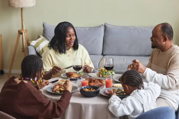 African family sitting at dining table eating and talking during holiday dinner in living room