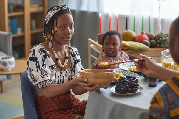 African woman suggesting traditional food for her family while they having dinner together at table at home