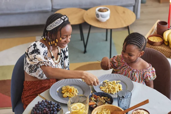 两个身穿民族服装的非洲女孩在房间的餐桌边吃传统食物 — 图库照片