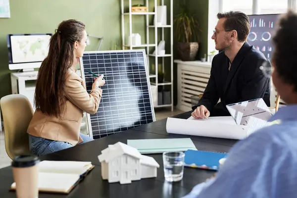 会議で彼女の同僚に新しいソーラーパネルを提示する若い実業家 彼らはチームで代替エネルギーを議論 — ストック写真
