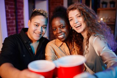 Neşeli güzel kızlar plastik bardaklarla şıngırdıyor ve evde dikilip eğlenirken kameraya bakıyorlar.