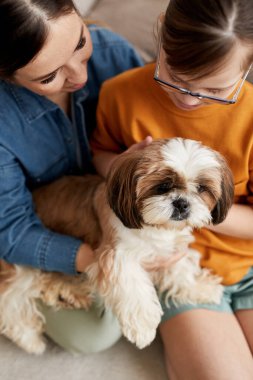 Anne ve kızının dikey portresi. Down sendromu var. Yerde şirin bir köpekle oynuyor.
