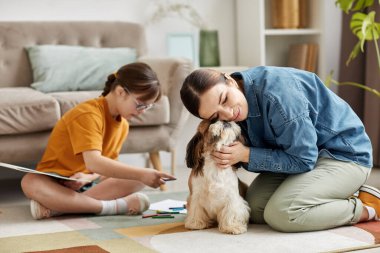Evde aile portresi, yerde sevimli küçük bir köpekle oynayan anne ve kız.