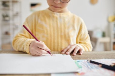 Minimal cropped shot of young girl drawing pictures while sitting at desk at home clipart