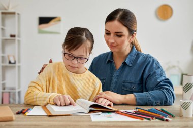 Evde öğrenim görürken Down sendromlu anne ve kızının birlikte kitap okuduğu portre.
