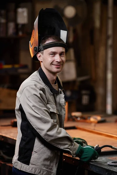 Vertical portrait of young male welder smiling at camera in industrial factory workshop