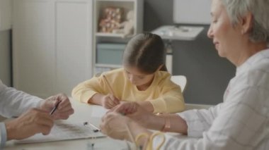 Yetişkin beyaz erkek çocuk uygulayıcısı küçük Asyalı kıza ilaç yazıyor. Annesiyle birlikte parlak, modern ofisinde doktoru ziyaret ediyor.