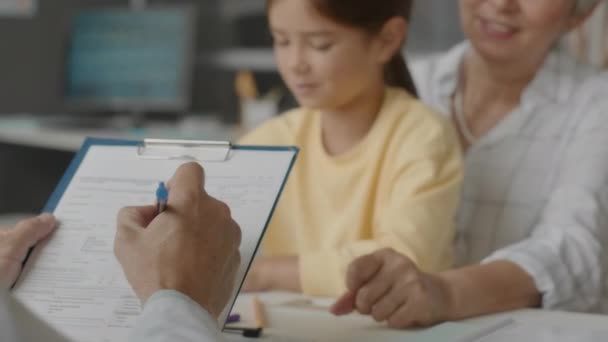 Nierozpoznawalny Pediatra Wypełniający Dokument Medyczny Udzielając Konsultacji Lekarskiej Małej Azjatce — Wideo stockowe