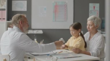 Yetişkin beyaz erkek doktorların bel ölçümleri. Küçük Asyalı kız ve annesinin vücut ısısı. Ofisteki randevusu sırasında temassız kızılötesi termometreyle.