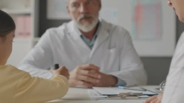 성숙한 코카서스 소아과 의사가 사무실에서 약속하는 환자와 그녀의 부모에게 시럽을주는 — 비디오