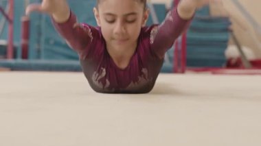 Mor mayo giymiş güzel bir kız dans sınıfında yerde yatar ve ritmik jimnastik yarışmasına hazırlanırken kollarını, bacaklarını ve vücudunu uzatır.