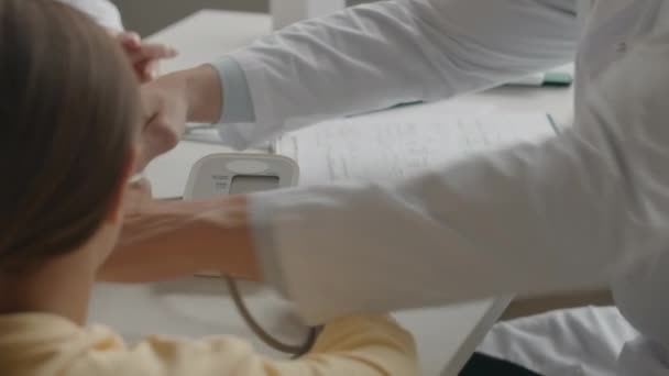 病院での診察任命中に少女の血圧を測定する認識できない男性小児科医の肩越し — ストック動画