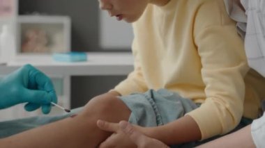 Küçük Asyalı kız ve şefkatli annesi kızların dizlerine üflerken doktor da yaralandıktan sonra pamuğa iyot sürmüş.