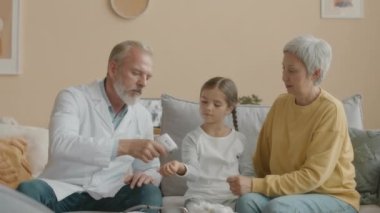 Orta boy beyaz erkek doktor, annesiyle birlikte küçük Asyalı kızın sıcaklığını ölçerken temas kurulamayan kızılötesi termometre kullanıyor.