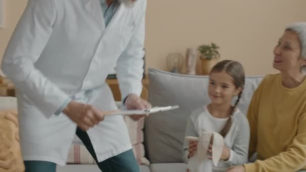 アジアの少女と母親を自宅に訪問する白いラボコートで成熟した白人男性小児科医のメディアショット — ストック動画