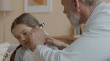 Yetişkin beyaz erkek otolarolog göğüs hizasında. Küçük Asyalı kızın evini ziyaret eden kulaklarını inceliyor.