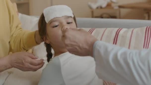 无法辨认的男医生用勺子把药水给发烧的小女孩 她躺在妈妈的膝上 额头上铺着洗涤布 — 图库视频影像