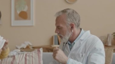 Kafkas erkek çocuk doktorunun ev ziyareti sırasında küçük Asyalı kızı steteskopla muayene ederken orta boy fotoğrafı.