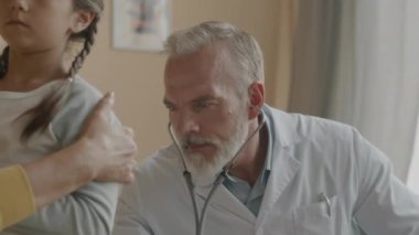 Ev ziyareti sırasında küçük kızı muayene ederken steteskop kullanan profesyonel beyaz erkek çocuk doktorunun göğüs röntgeni.