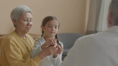 Tanımlanamayan erkek doktorun beline, evde tıbbi muayene sırasında annesinin kucağında oturan Asyalı küçük kıza bir şişe hap vermesi.