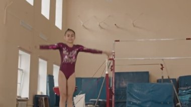 Mor taytlı küçük melez kızın yavaşlığı sınıfta artistik jimnastik yaparken kameraya sıçrama yapıyor.