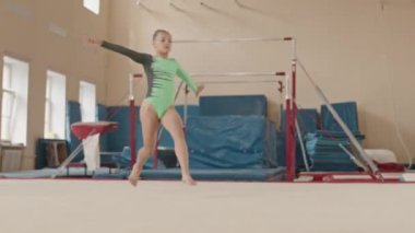 Taytlı, beyaz kadın jimnastikçinin yavaşlaması sınıftaki jimnastik eğitimi sırasında atlama ve diğer sanatsal öğeler üzerinde pratik yapıyor.