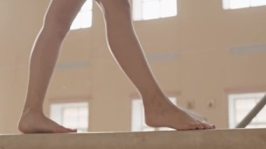 Jimnastik sınıfında denge kirişinde dikkatle yürüyen tanınamayan küçük kızların düşük kesimi.